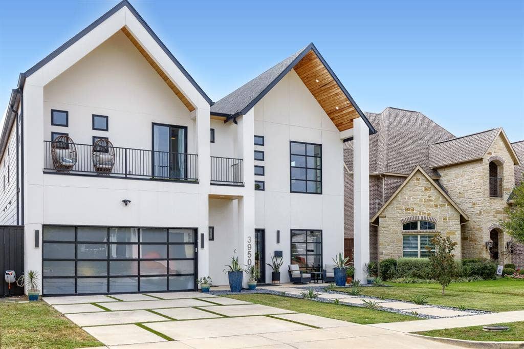3950 Beechwood Lane, Dallas, TX 75220 Modern facade with a peaked roofline, wood-finish eaves, a balcony with black railings, a glass panel garage door, and a concrete paver driveway