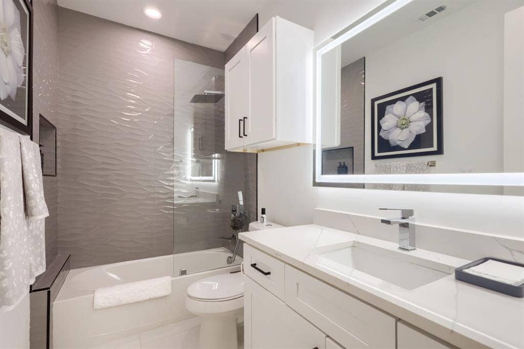 3950 Beechwood Lane, Dallas, TX 75220 Built-in bathtub with glass shower enclosure, wave-textured tile surround, vanity with integrated sink, chrome faucet, and illuminated mirror