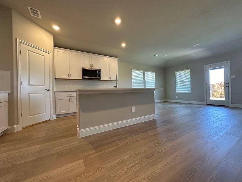 Spacious open-concept living area with wood-finish flooring, recessed lighting, and a kitchen featuring white cabinetry, a built-in microwave, and a breakfast bar
