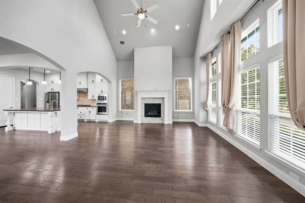 911 Midland Drive, Allen, TX 75013 Vaulted ceiling with recessed lighting, wood-finish flooring, two-story windows with blinds, built-in fireplace with white mantel, kitchen island with pendant lighting