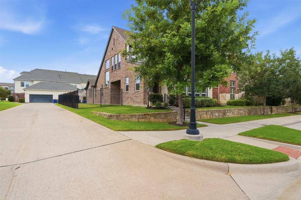 911 Midland Drive, Allen, TX 75013 Brick exterior, gabled roofline, stone retaining wall, wrought iron fencing, concrete driveway