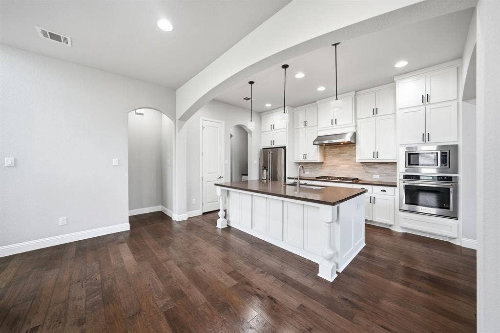 911 Midland Drive, Allen, TX 75013 Wood-finish flooring throughout, white shaker cabinetry, stainless steel appliances, kitchen island with built-in sink, and recessed lighting