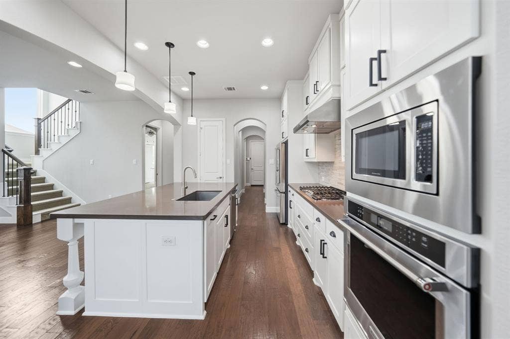 911 Midland Drive, Allen, TX 75013 Gourmet kitchen with stainless steel appliances, dark wood-finish flooring, recessed lighting, white cabinetry, and an expansive island featuring a built-in sink and pendant lighting