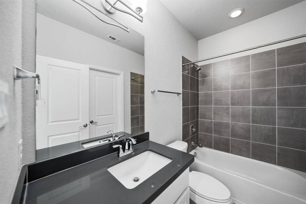 911 Midland Drive, Allen, TX 75013 White drop-in sink, dark countertop, chrome fixtures, built-in tub with tile surround, and recessed lighting