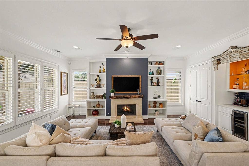 5542 Monticello Avenue, Dallas, TX 75206 Living area featuring a fireplace with a mantel, built-in shelving, wood-finish flooring, a ceiling fan, and plantation shutters