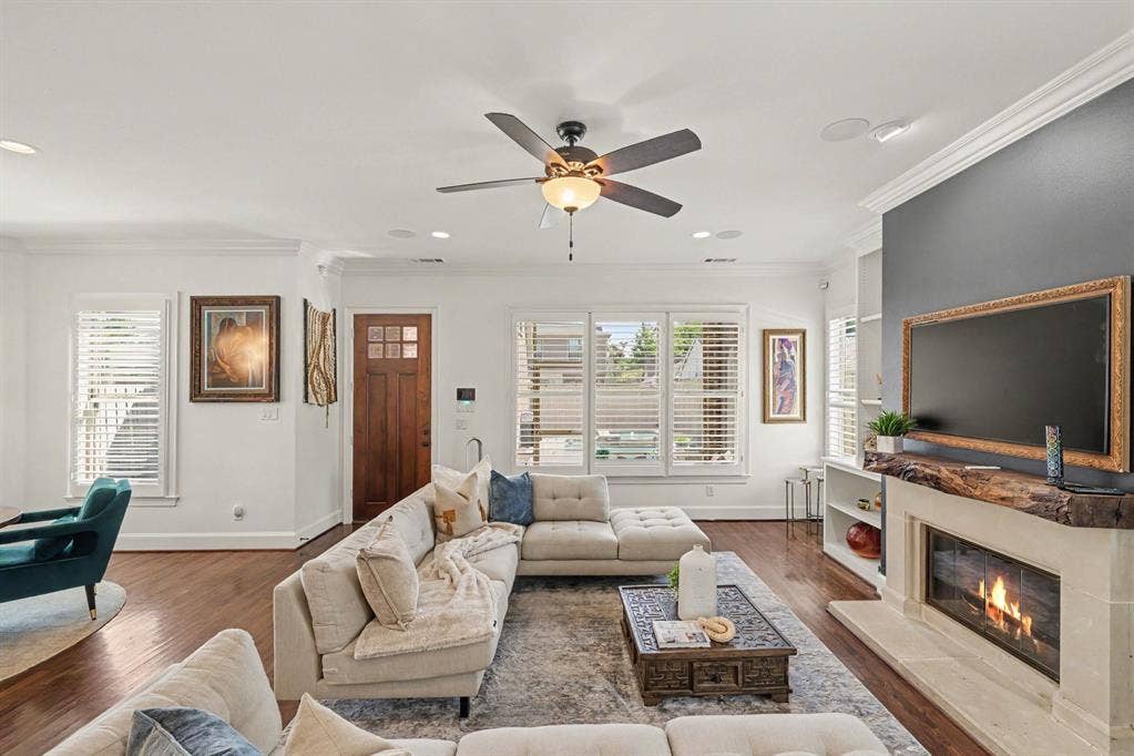 5542 Monticello Avenue, Dallas, TX 75206 Hardwood flooring, crown molding, ceiling fan, natural light from multiple windows, and a built-in fireplace with a stone surround