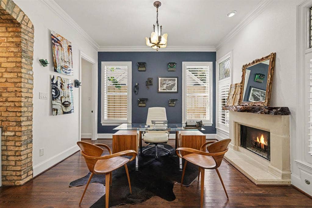 5542 Monticello Avenue, Dallas, TX 75206 Hardwood flooring throughout, featuring a brick archway, a built-in fireplace with a stone surround, windows with louvered shutters, and a ceiling-mounted light fixture