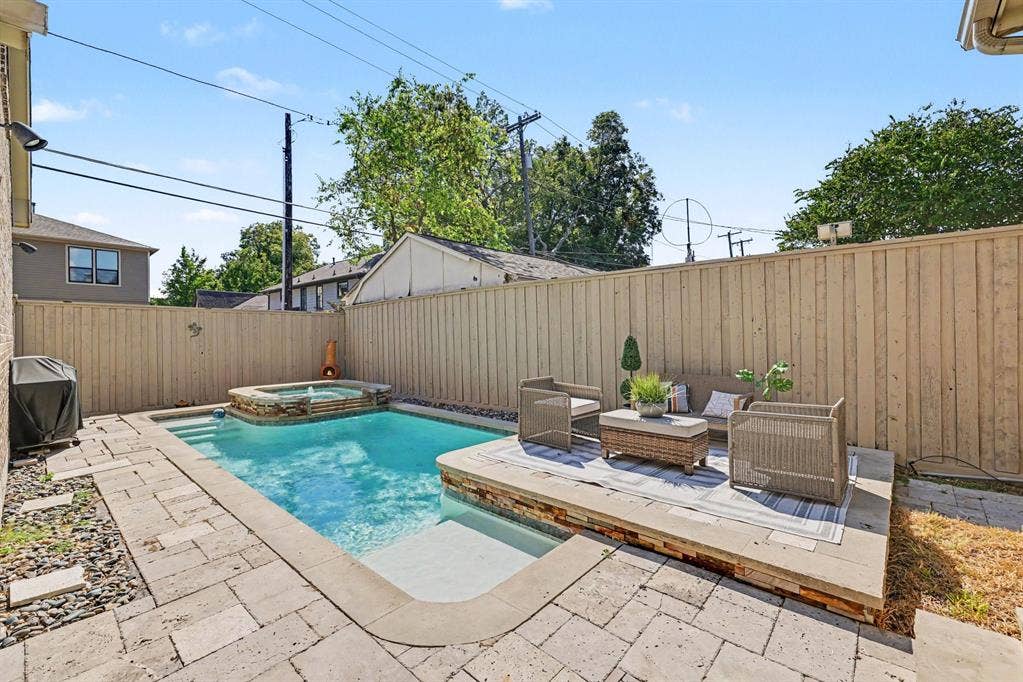5542 Monticello Avenue, Dallas, TX 75206 Outdoor pool with integrated spa and stone surround, accompanied by an elevated patio area and wood privacy fencing
