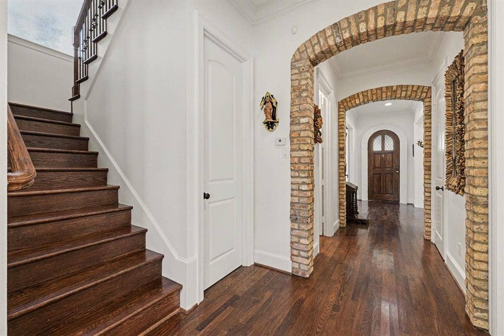 5542 Monticello Avenue, Dallas, TX 75206 Wood-finish flooring throughout, brick archways, white paneled doors, and a staircase with dark wood treads and an ornate railing