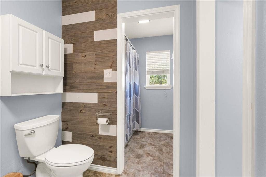 White toilet with chrome hardware, wood-finish accent wall, and built-in white cabinetry