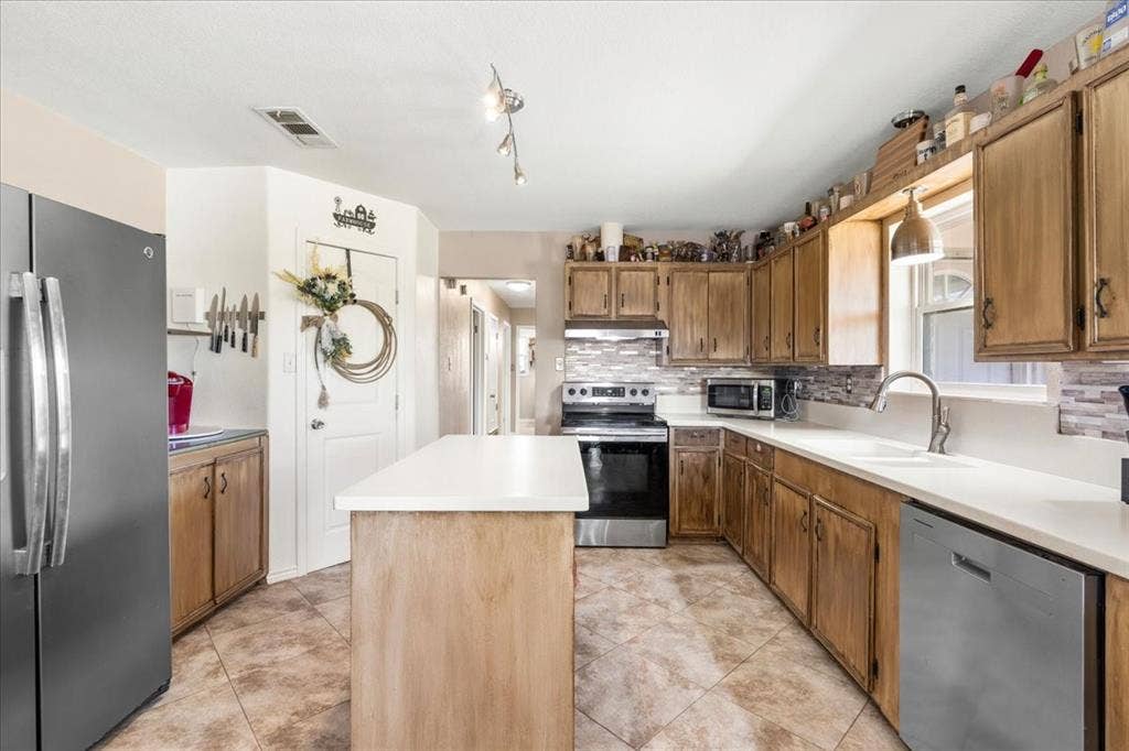 Kitchen featuring wood cabinetry, stainless steel appliances, white countertops, tile flooring, and a central island