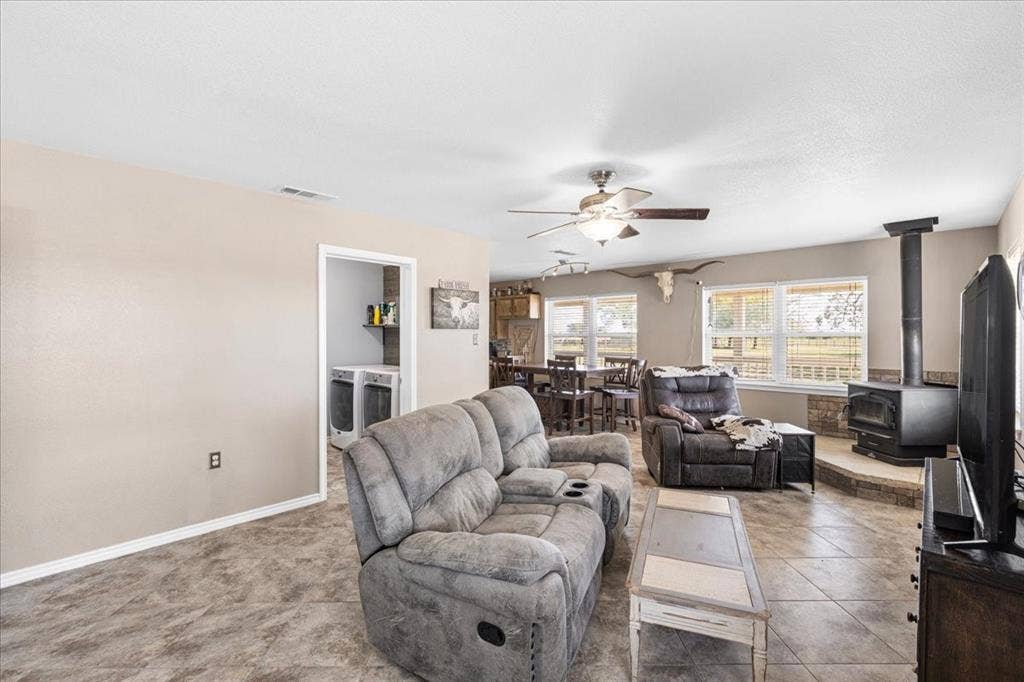 Spacious living area featuring tile flooring, a built-in wood-burning stove with a stone surround, and multiple windows
