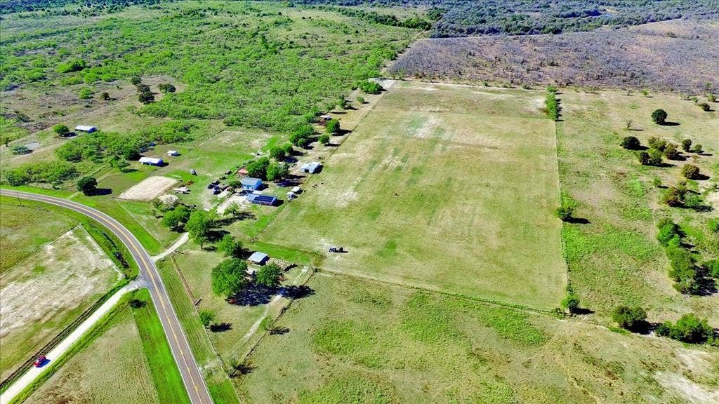 Expansive land parcel featuring open fields, scattered trees, and a visible road frontage