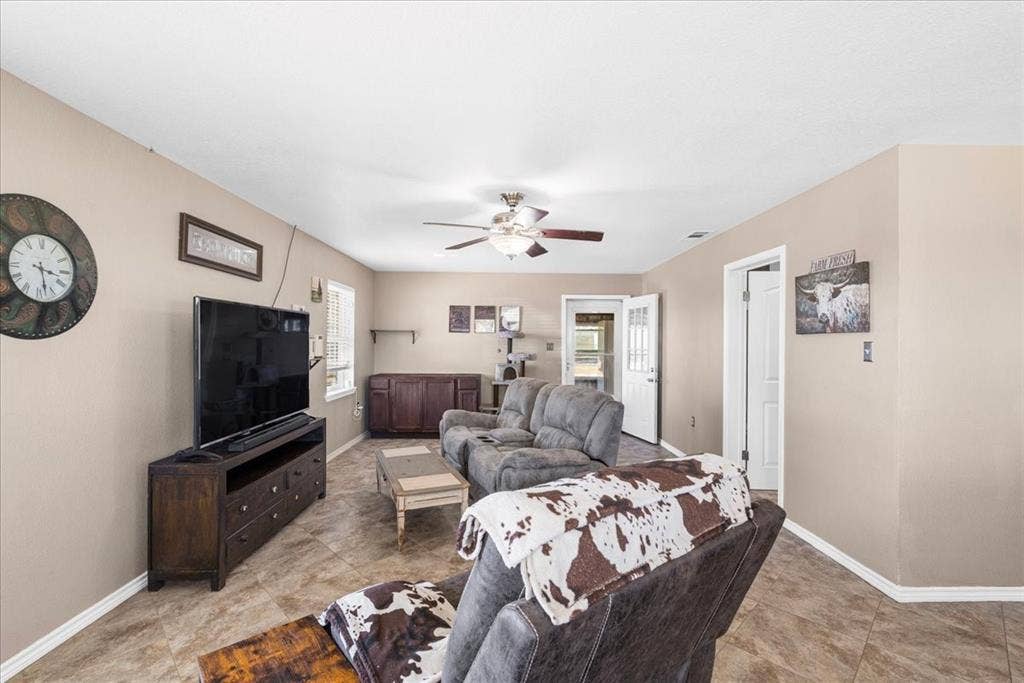 Spacious living area featuring neutral-toned walls, tile flooring, a ceiling fan, and a window with blinds