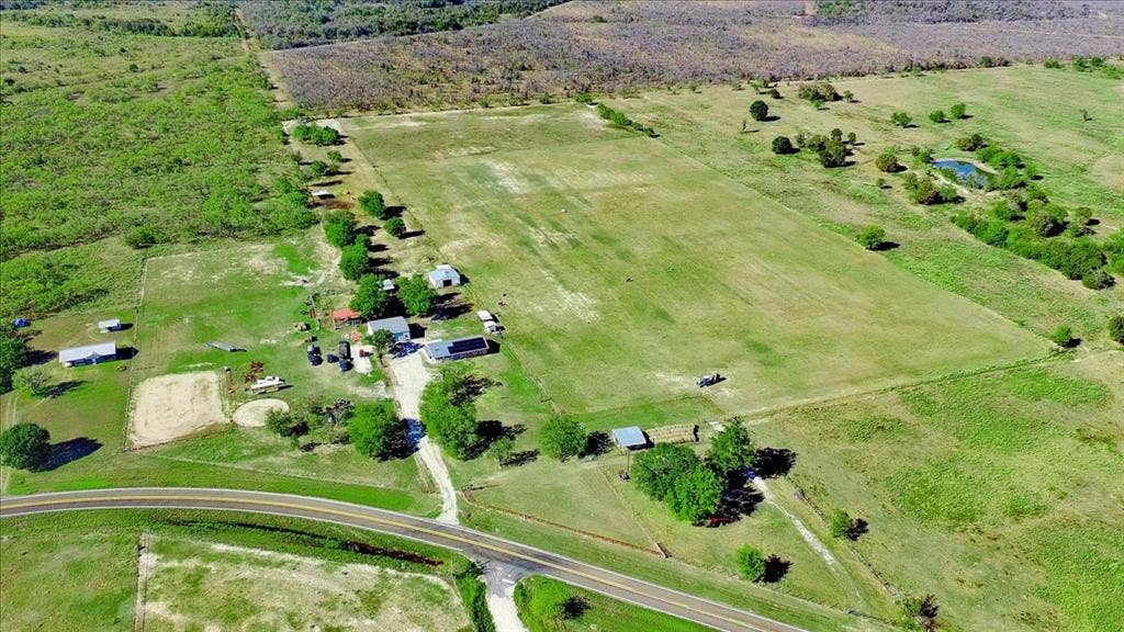 Expansive rural property featuring multiple outbuildings, open fields, and a private pond