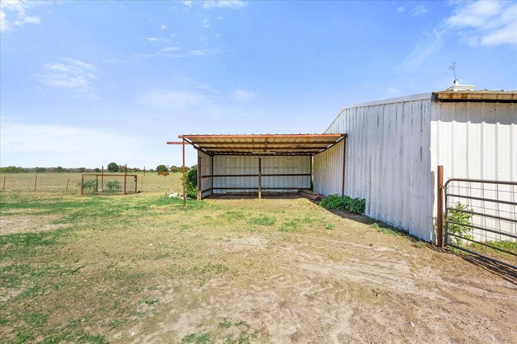 Metal building with an attached covered structure, expansive open field, and perimeter fencing