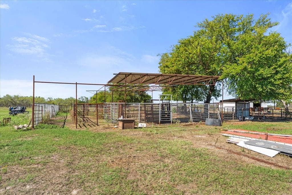 Expansive fenced paddock with a partial shade structure, multiple pens, and a large mature tree