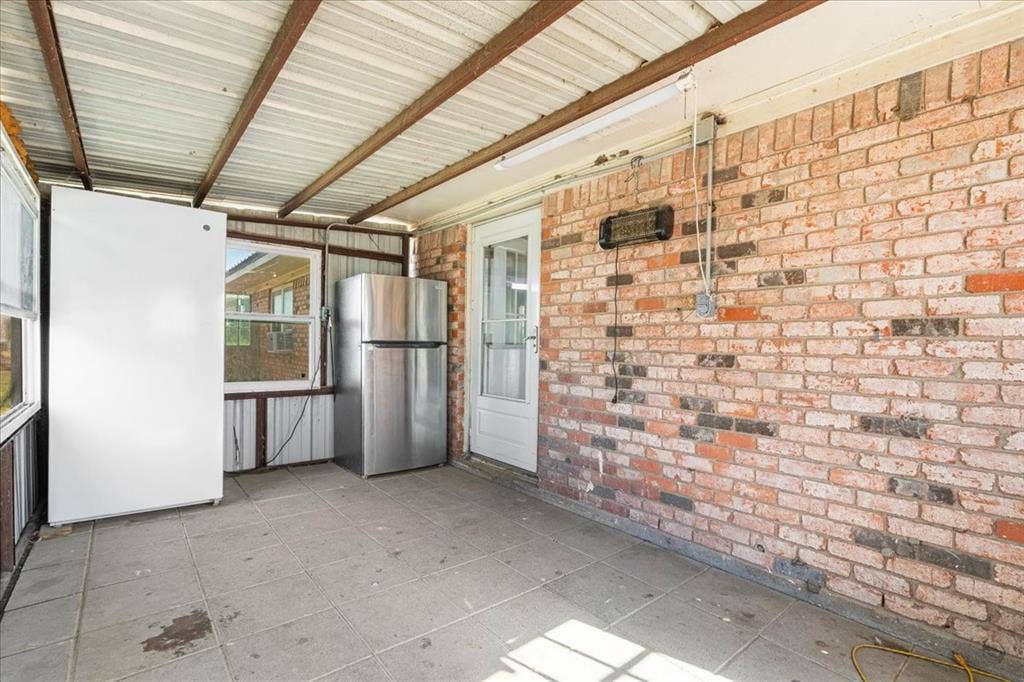 Screened-in porch featuring a brick exterior wall, tile flooring, and a corrugated metal roof