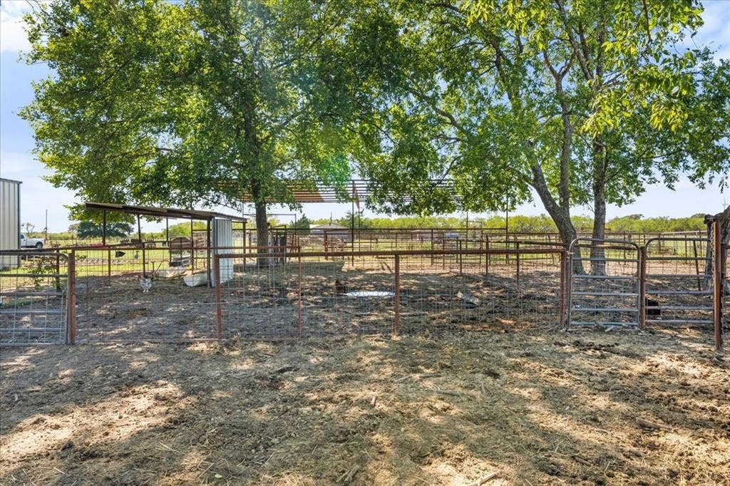 Fenced outdoor enclosure with multiple gated sections, mature trees, and a covered structure