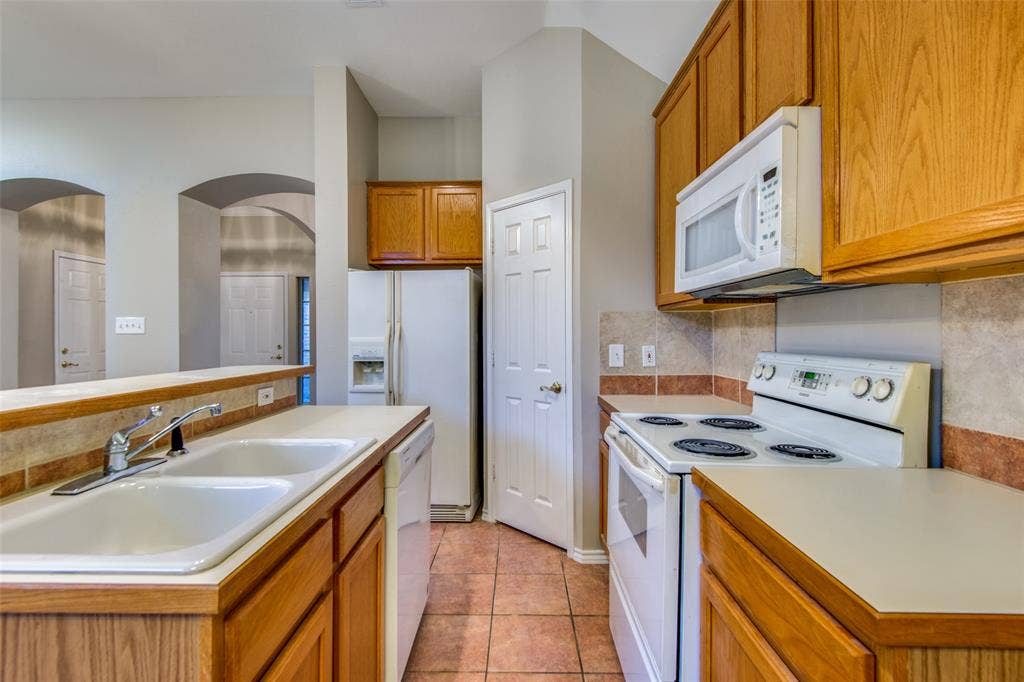 1913 Piney Creek Boulevard, Denton, TX 76205 Kitchen featuring wood-finish cabinetry, tile flooring, and integrated white appliances