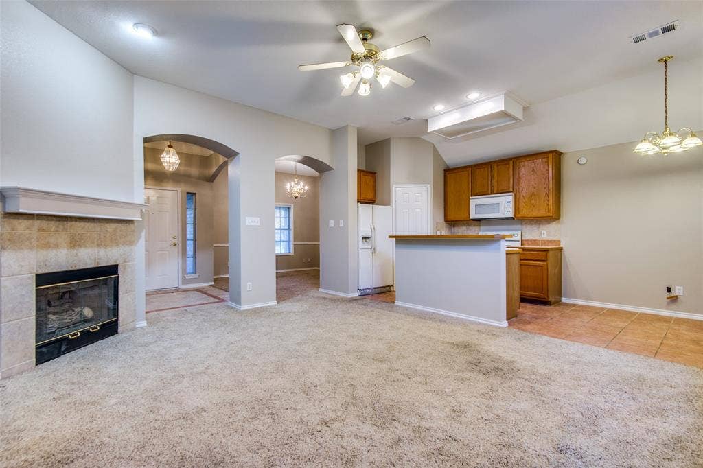 1913 Piney Creek Boulevard, Denton, TX 76205 Tiled fireplace surround with mantel, arched doorways, kitchen with wood cabinetry, white appliances, and a breakfast bar, and vaulted ceilings with a ceiling fan
