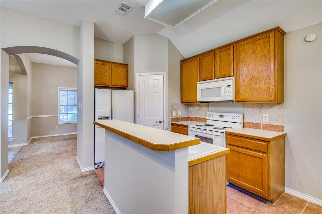 1913 Piney Creek Boulevard, Denton, TX 76205 Kitchen featuring wood cabinetry, white appliances, and a breakfast bar