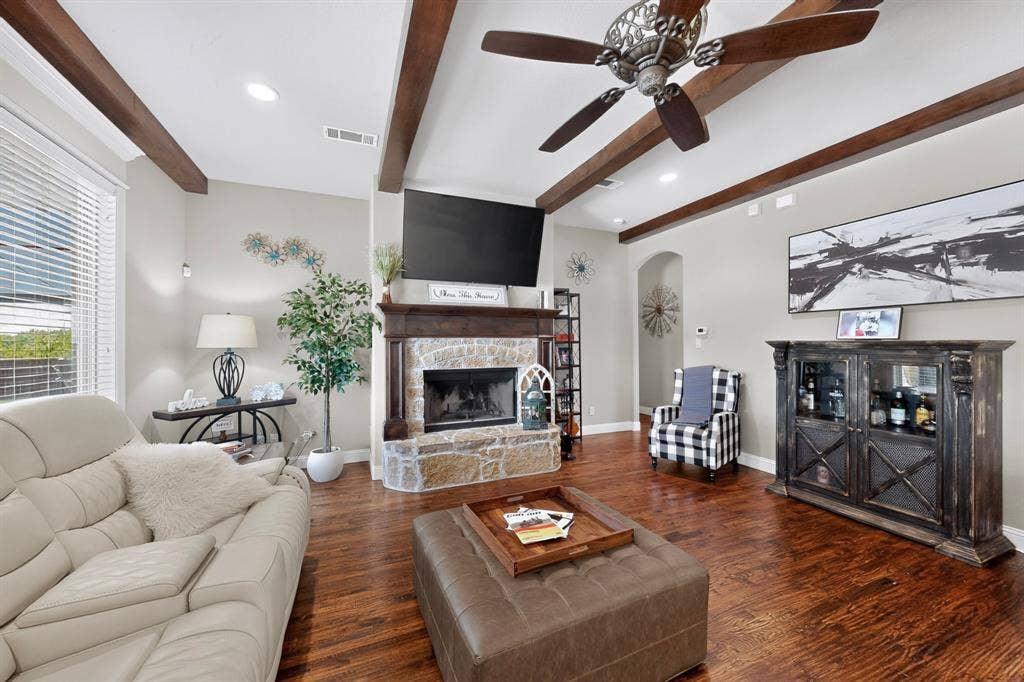 5020 Lindy Court, Midlothian, TX 76065 Spacious living area featuring exposed wood beam ceiling details, a wood-finish plank floor throughout, and a fireplace with stone surround