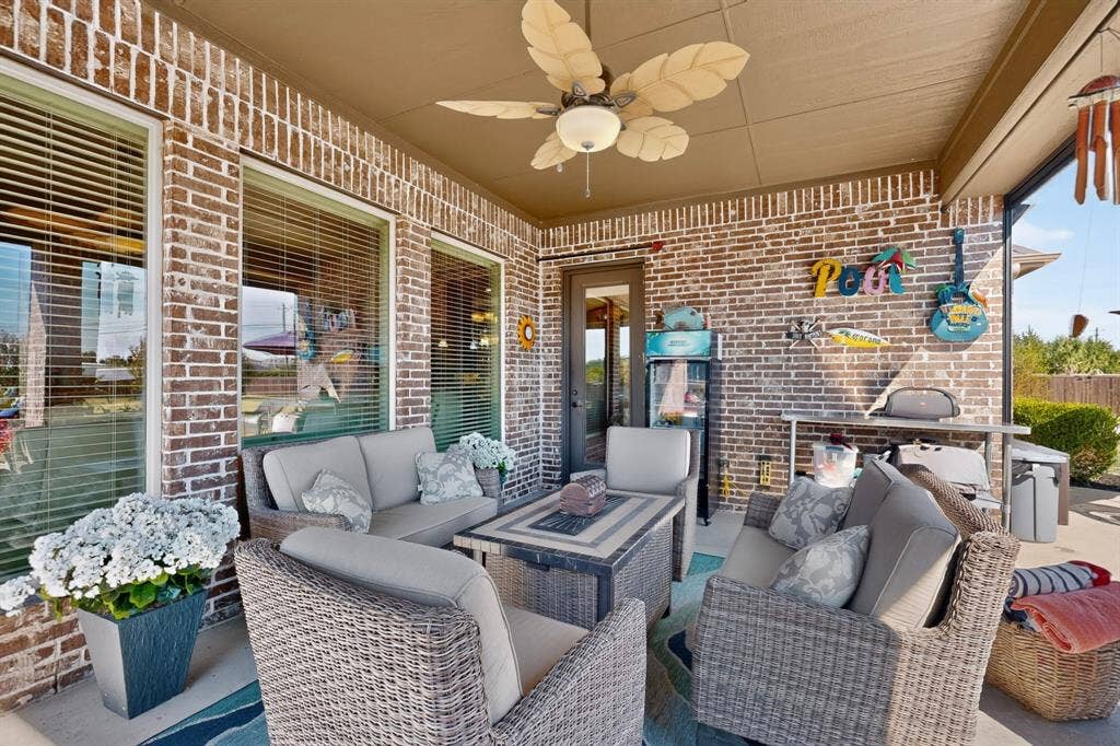 5020 Lindy Court, Midlothian, TX 76065 Covered porch with brick exterior featuring comfortable wicker seating, a fire table with metal frame, ceiling fan with integrated lighting, and large windows allowing natural light throughout the space