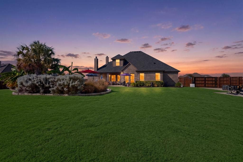 5020 Lindy Court, Midlothian, TX 76065 Elegant brick residence with hipped roofline and illuminated interior showcasing multiple windows