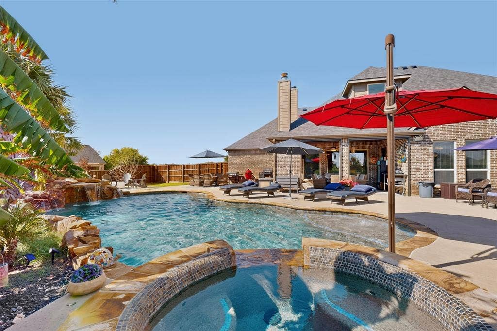 5020 Lindy Court, Midlothian, TX 76065 Lagoon-style swimming pool with rock waterfall feature, integrated spa with mosaic tile, and extensive concrete patio