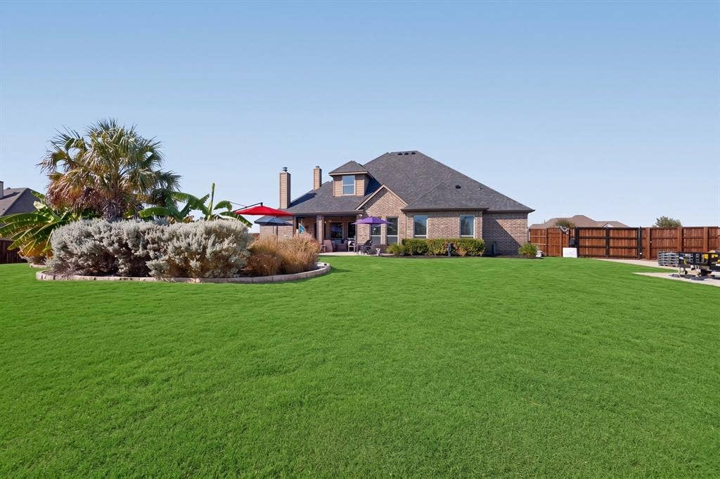 5020 Lindy Court, Midlothian, TX 76065 Expansive green lawn, brick exterior, dark-toned roof, paved patio, and wood privacy fencing