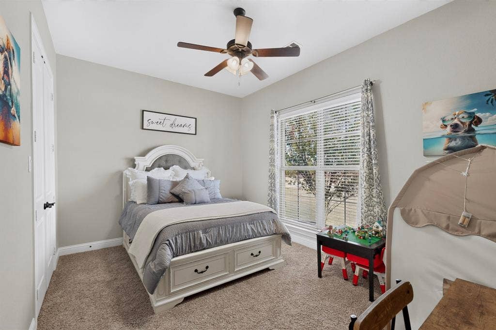 5020 Lindy Court, Midlothian, TX 76065 Carpeted flooring, ceiling fan with light fixture, window with blinds and patterned drapes, white paneled door with black hardware, and light-toned walls