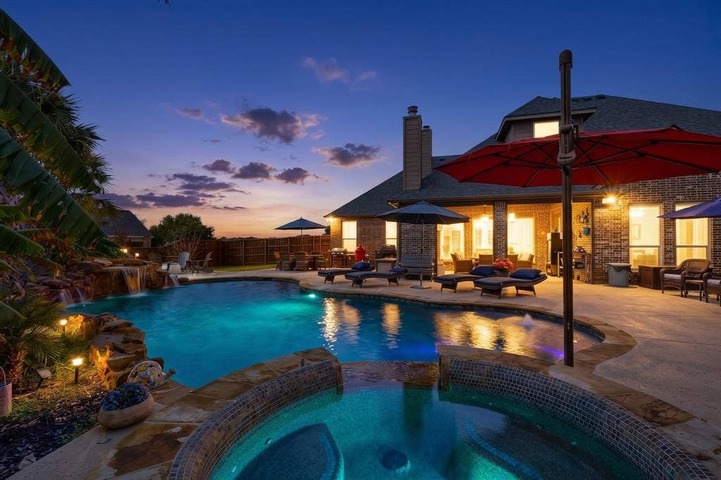 5020 Lindy Court, Midlothian, TX 76065 Custom-shaped swimming pool with an integrated spa, rock waterfall feature, and surrounding concrete patio