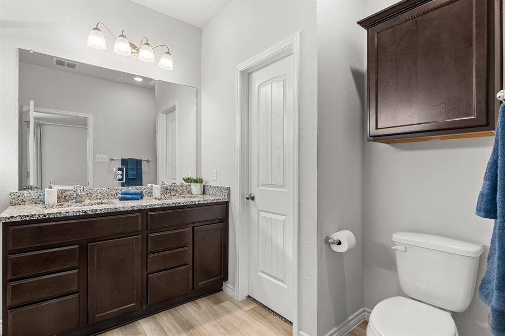 Dual vanity with undermount sinks, granite-patterned countertop, dark wood-finish cabinetry, and wood-finish flooring