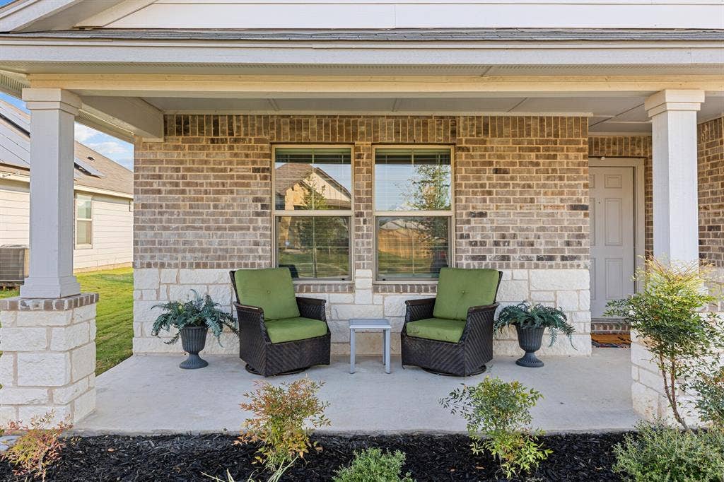Covered front porch featuring brick and stone veneer, concrete flooring, and white columns
