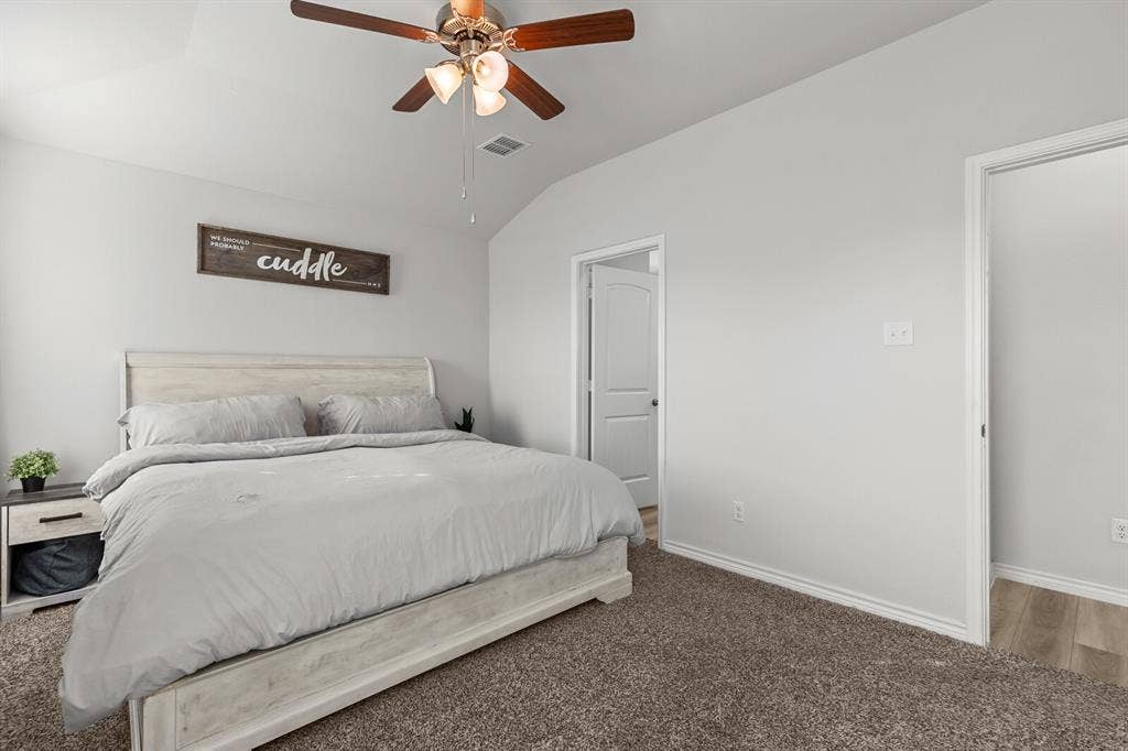 Vaulted ceiling with a wood-finish ceiling fan, neutral wall paint, and plush carpeting