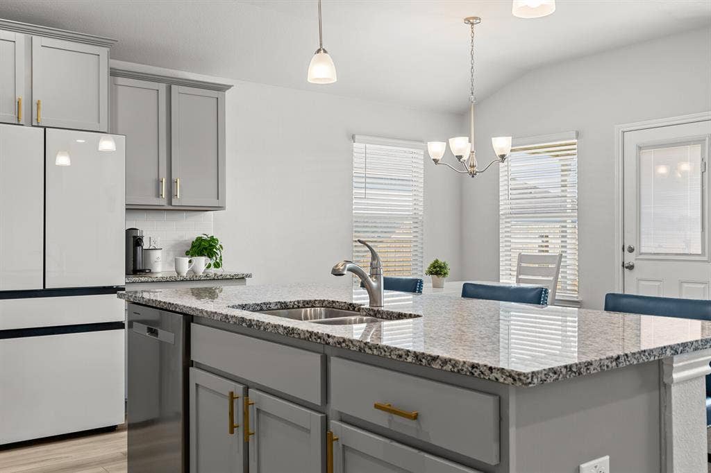 Kitchen featuring light gray cabinetry with gold-tone hardware, granite countertops, a stainless steel sink, and a built-in dishwasher