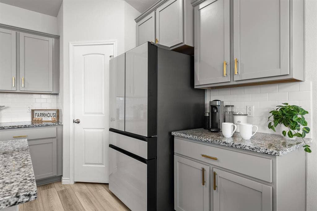 Gray cabinetry with gold-tone hardware, granite-style countertops, white subway tile backsplash, and wood-finish flooring