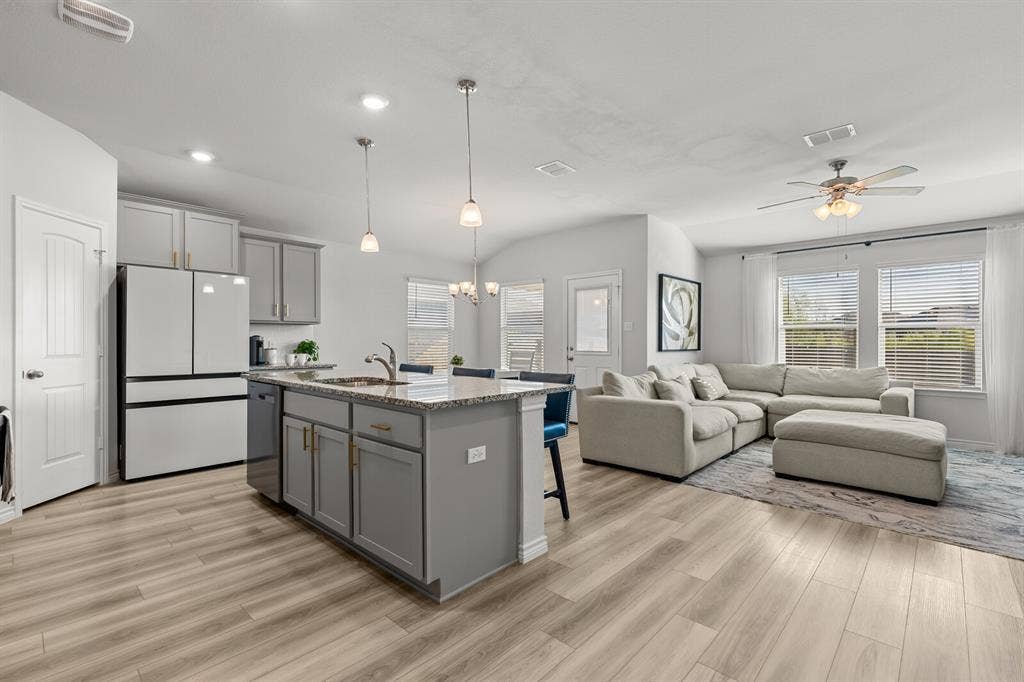 Open-concept layout featuring wood-finish flooring, a kitchen island with granite countertops, light gray cabinetry, and recessed lighting