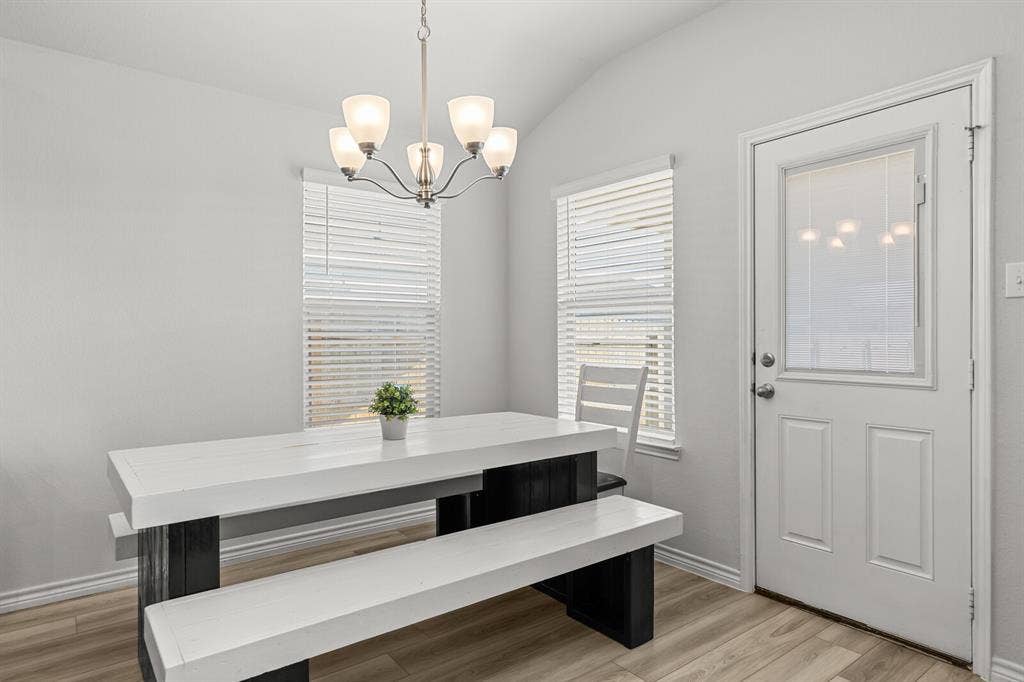 Vaulted ceiling with a five-light chandelier, two windows with blinds, wood-finish flooring, and a white paneled door with a privacy glass insert