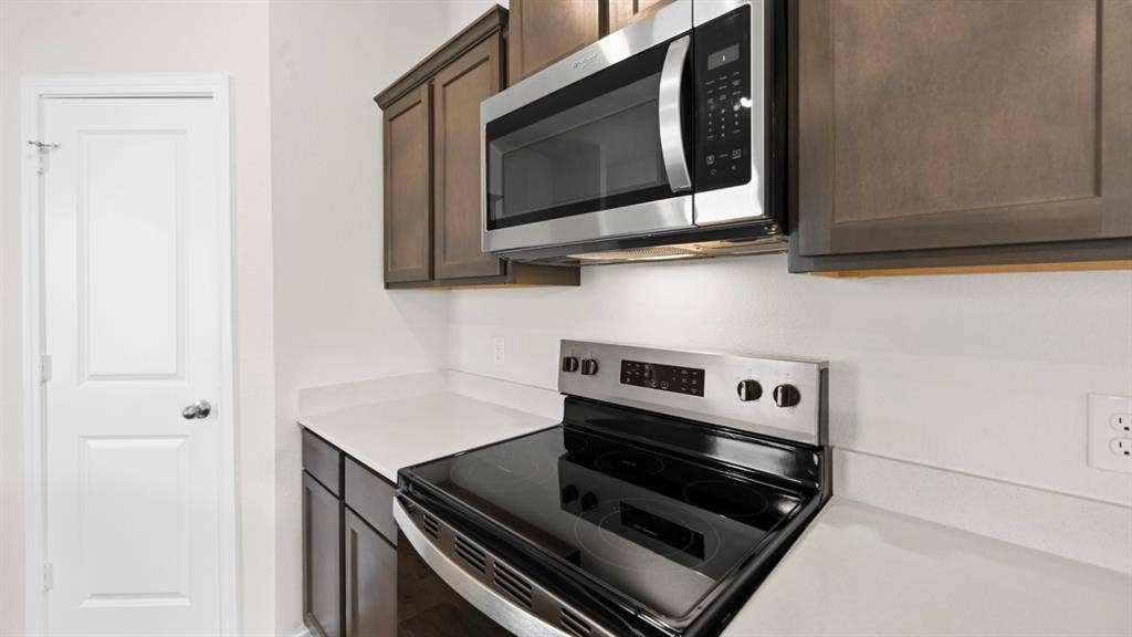 Stainless steel microwave, electric range with black cooktop, white countertops, and wood-finish cabinetry