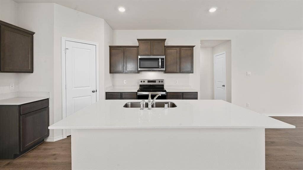 Kitchen featuring a central island with an undermount sink, dark wood-finish cabinetry, light countertops, and wood-finish flooring