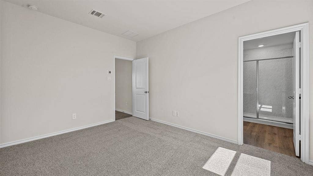 Carpeted flooring, neutral wall tones, and doorway access to an adjoining room with wood-finish flooring and a glass-enclosed shower