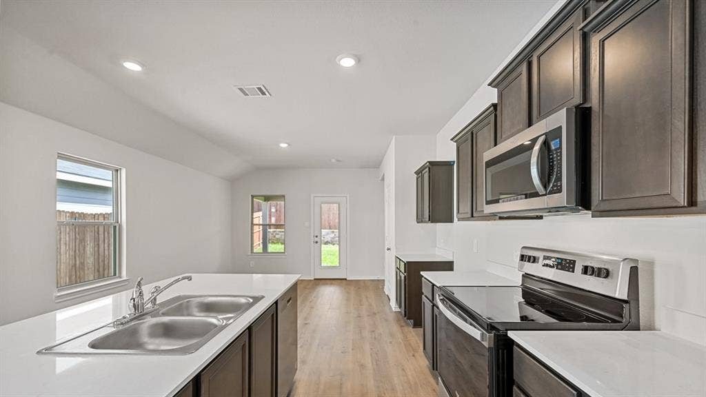Kitchen featuring dark wood-finish cabinetry, stainless steel appliances, a double basin sink, white countertops, and wood-finish flooring