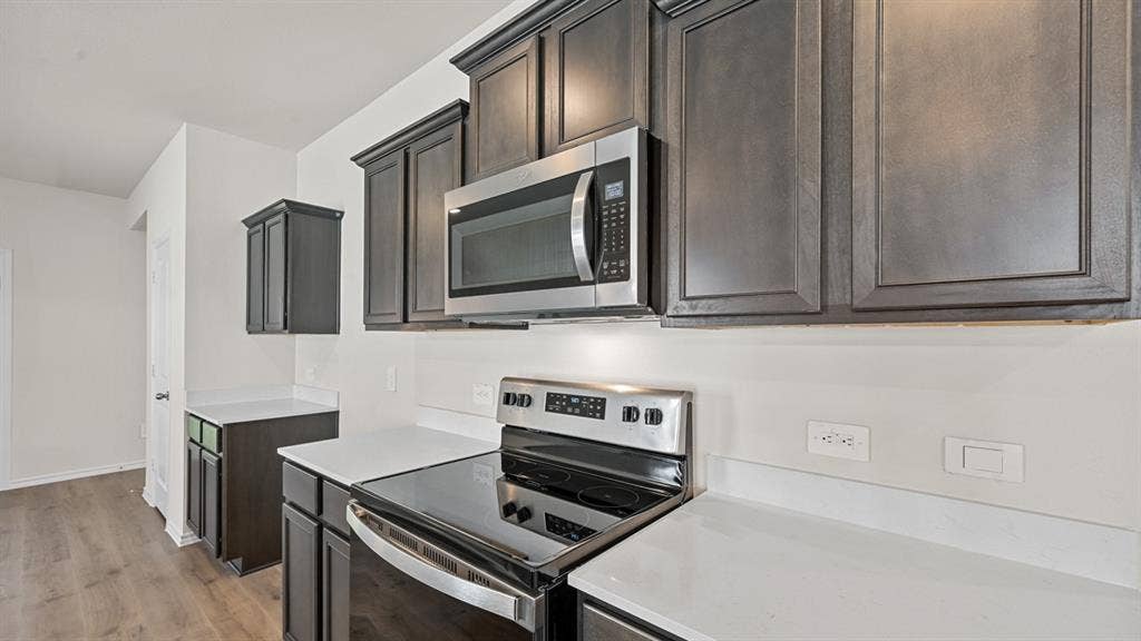 Dark wood-finish cabinetry, stainless steel microwave, electric range, and light-toned countertops
