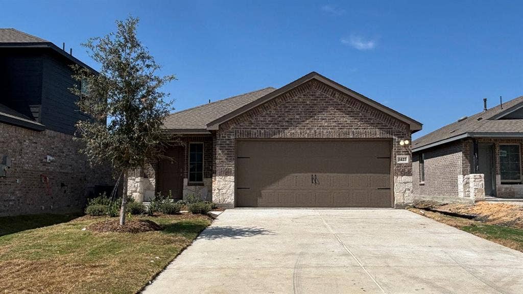 Brick exterior with stone accents, attached garage, concrete driveway, and a front entry