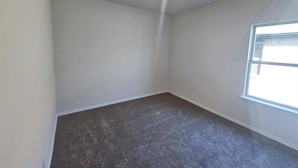 Bright room featuring neutral wall paint, gray patterned carpet, a single window, and white baseboards