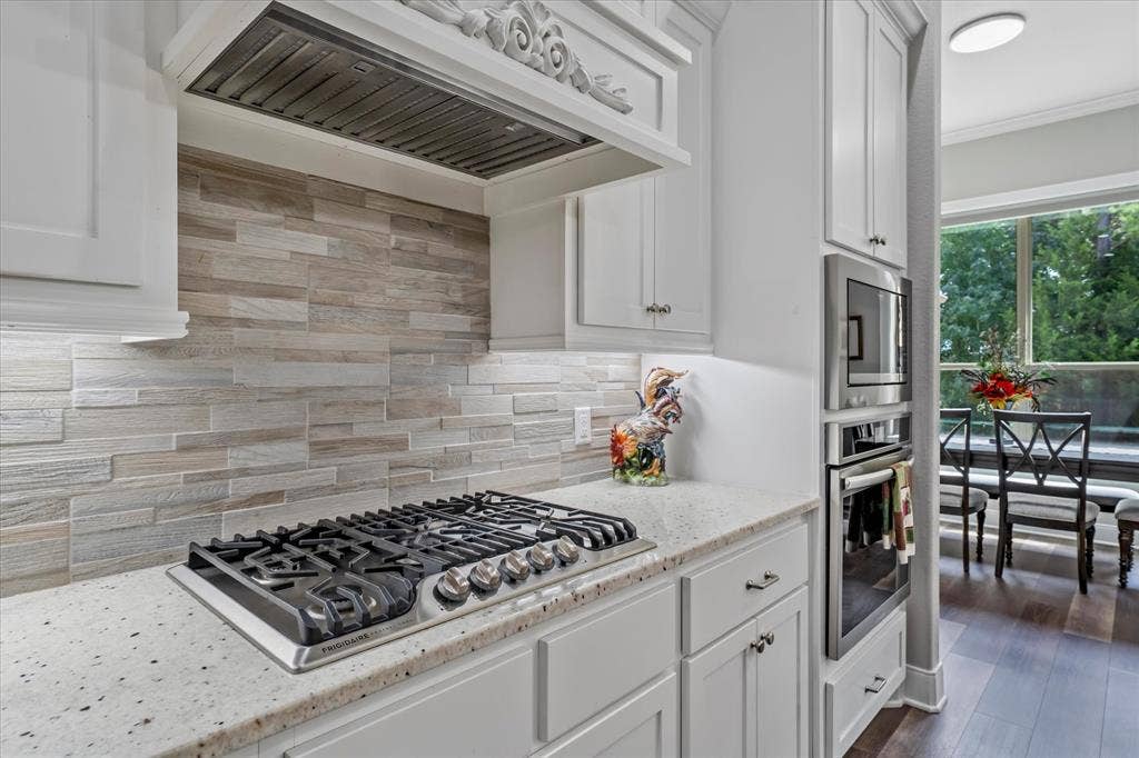 14486 Meadow Glen, Lindale, TX 75771 White cabinetry, integrated gas cooktop, light-toned stacked stone backsplash, white speckled countertop, and stainless steel built-in appliances