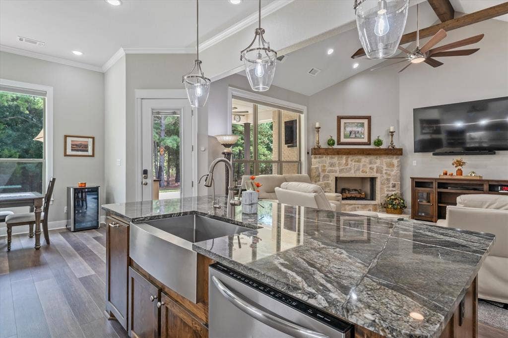 14486 Meadow Glen, Lindale, TX 75771 Vaulted ceiling with exposed wood beams, stone fireplace, wood-finish flooring, central island with an undermount stainless steel sink, and pendant lighting
