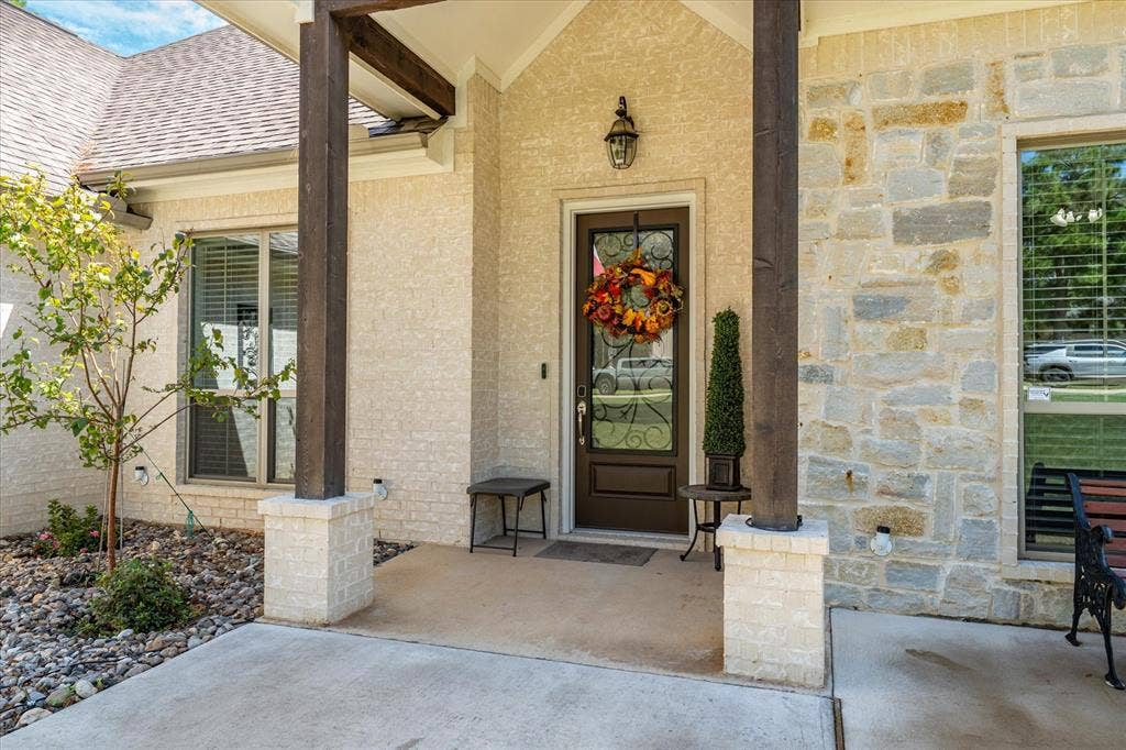 14486 Meadow Glen, Lindale, TX 75771 Covered front entry featuring stone and stucco exterior, wood support columns, and a solid wood entry door with decorative glass
